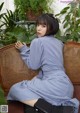 A woman sitting on a wicker chair in a room with plants.