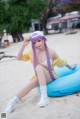 A woman with long purple hair sitting on an inflatable ring on the beach.