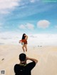 A man taking a picture of a woman standing in the sand.