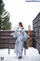 A woman in a blue and white kimono standing in the snow.