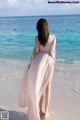 A woman in a pink dress standing on the beach.