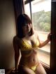 A woman in a yellow bikini standing by a window.