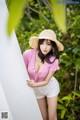 A woman in a straw hat leaning against a wall.