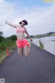 A woman in a pink sports bra top and pink shorts jumping in the air.