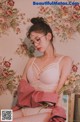 A woman wearing glasses and a pink robe sitting on a bed.