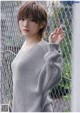 a woman wearing a gray sweater standing in front of a fence