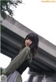 A woman standing in front of a bridge wearing a green jacket.