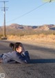 A woman laying on the side of the road with her head in her hands.