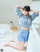 A woman in a gray sweatshirt and blue shorts posing on a bed.