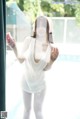 A woman in a white shirt and white tights standing by a pool.
